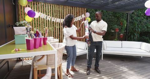 Couple Exchanging Long Wrapped Gift on Decorated Patio During Backyard Birthday Celebration