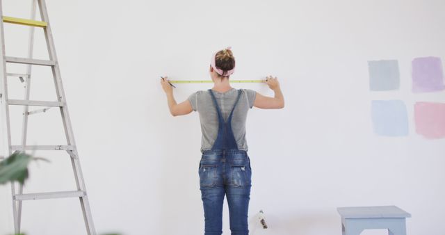 Caucasian woman measuring walls with ruler at ladder. Lifestyle, domestic life, house interior and work, unaltered.