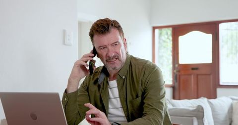 Middle-aged man telecommuting with smartphone and laptop