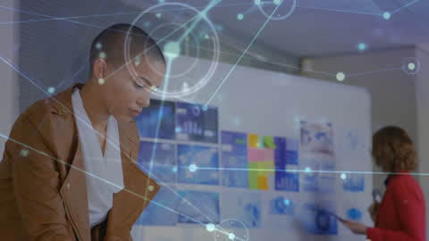 A biracial woman in a brown leather jacket is concentrating intently, surrounded by digital connections that represent information flow and technology integration. Another person in the background appears to be working collaboratively. This visual is ideal for projects emphasizing teamwork, digital communication, modern business environments, or innovative technology solutions. It is useful for illustrating concepts in business presentations or technology-driven content.