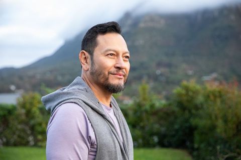 Mature asian man enjoying serene misty mountain view in casual hoodie and activewear