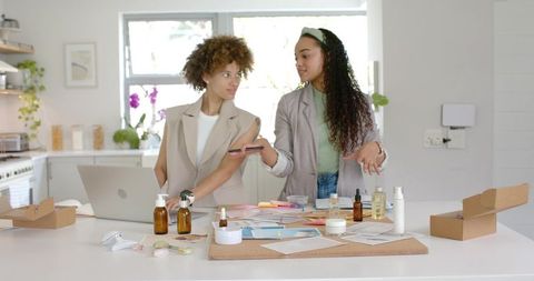 African american women planning skincare packaging and branding in bright kitchen studio