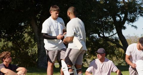 Multiracial cricket teammates practicing batting drills on grassy field, showing teamwork