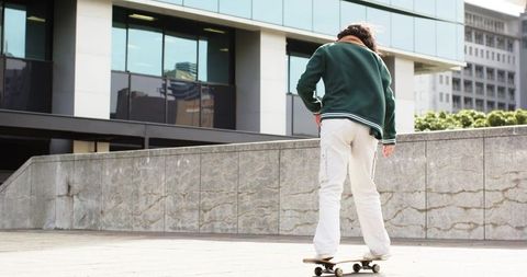 Young woman riding skateboard across modern urban plaza with glass facade backdrop