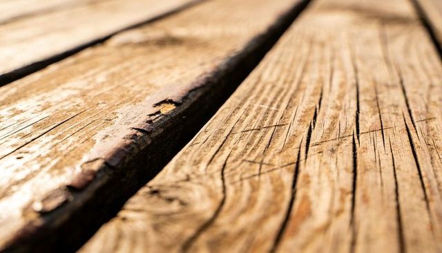 Sunlit weathered wood planks showing cracks, knots, grain and narrow gap texture