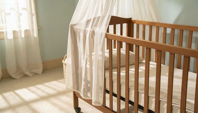 Sunlit wooden crib featuring sheer canopy and neutral bedding in pastel nursery