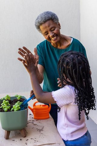 Senior african american woman high-fiving granddaughter planting herbs on sunlit patio