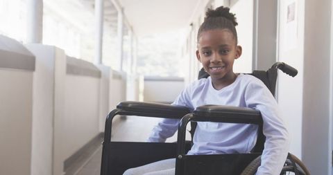 Joyful african american girl navigating hallway in wheelchair