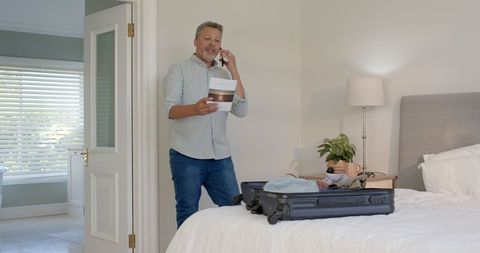 Man Packing Suitcase and Talking on Phone in Bedroom Before Travel
