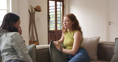 Two women chatting on sectional sofa in cozy living room, casual friendship moment