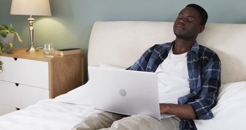 Man Relaxing on Bed with Laptop in Modern Bedroom