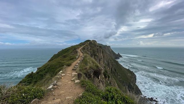 Hiking winding coastal ridge trail leading to dramatic rocky headland and ocean views