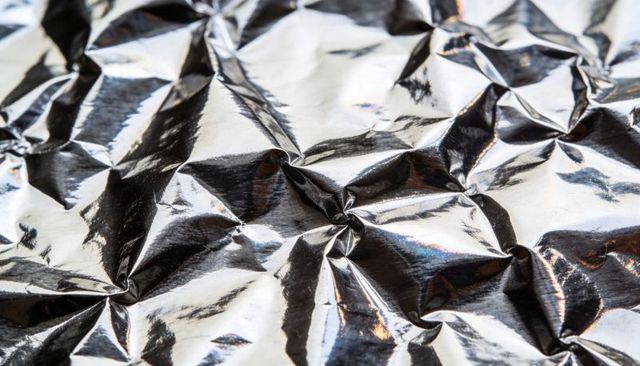 Crumpled aluminum foil reflecting studio light with iridescent highlights and sharp creases