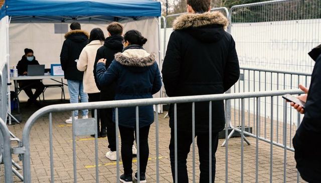 People queuing at outdoor screening tent wearing winter coats and face masks with barriers