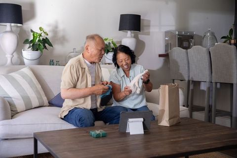 Chinese senior couple receiving gift while video calling on tablet in cozy living room