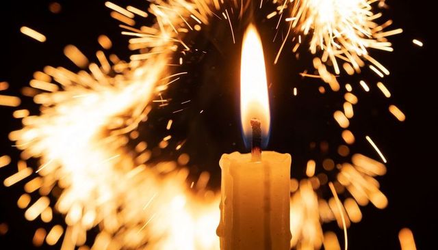 Burning candle flickering amid golden sparkler halo closeup macro warm glow