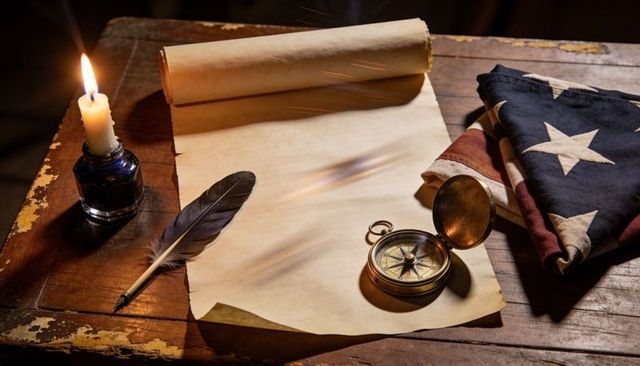 Candlelight illuminating parchment with quill and compass beside folded american flag