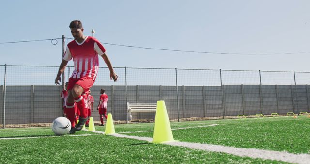 Young soccer player focusing on ball control while dribbling through cones on green field. Perfect for themes of sports training, youth development, athleticism, and outdoor activity ads or articles.