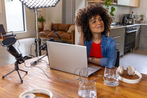 African american podcaster recording from home kitchen studio with laptop and microphone