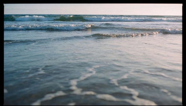 Calm pastel seascape with gentle surf and shallow shoreline foam lines during golden hour