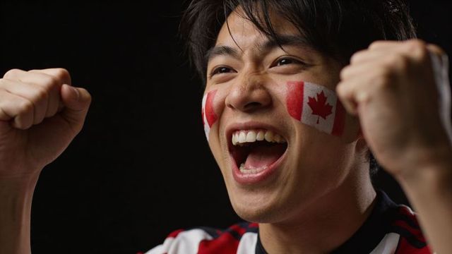 Asian canadian fan cheering with painted flag face and raised fists closeup portrait