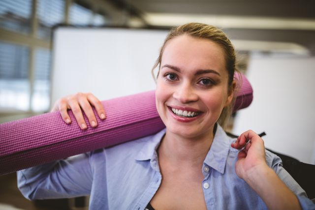 Portrait of happy businesswoman with bag and exercise mat in meeting room at creative office