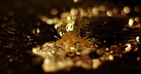 Golden snowflake rotating over falling liquid in festive mood lighting