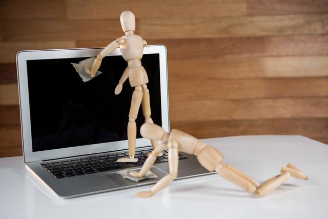 Wooden mannequins are cleaning a laptop screen and keyboard, symbolizing the importance of maintaining clean and functional technology. This image can be used in articles about computer maintenance, office hygiene, teamwork, or conceptual pieces on technology care.
