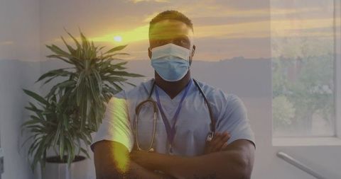 Masked clinician standing with arms crossed and stethoscope, sunset glow double exposure