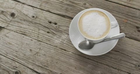 Cappuccino cup resting on rustic wooden table with spoon and generous copy space