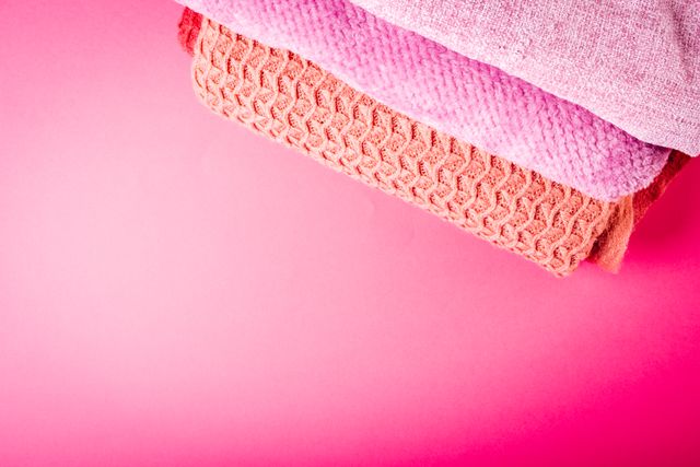 Colorful textiles neatly stacked on a vibrant pink surface. Ideal for use in articles or adverts related to clothing, textiles, fabric shopping, fashion design, or home decor. The bright background highlights various textures and patterns, creating a visually appealing display.