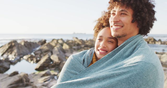African american couple wrapped in blanket standing on the rocks near the sea - Download Free Stock Photos Pikwizard.com