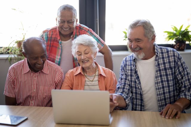 Group of happy senior people gathered around a laptop, smiling and engaging with technology. Ideal for use in articles or advertisements about senior living, technology for the elderly, social activities in nursing homes, or promoting digital literacy among older adults.