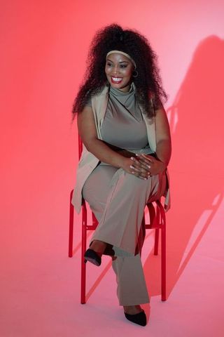 Confident african american woman sitting on red chair, posing in beige fashion outfit