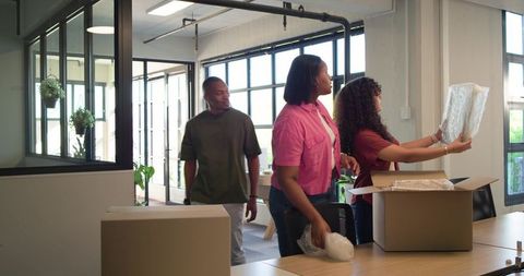 Multiracial team unpacking boxes, organizing modern office workspace with bubble wrap