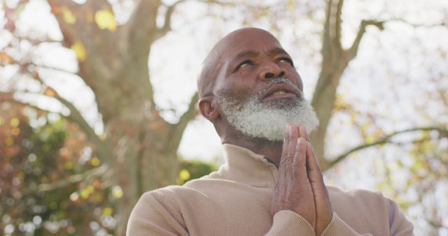 Image of thoughtful senior african american man holding hands in prayer in garden. Retirement, faith, inclusivity, health and happiness concept digitally generated image.