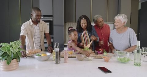 Multi-generational family preparing fresh salad together at modern marble kitchen island