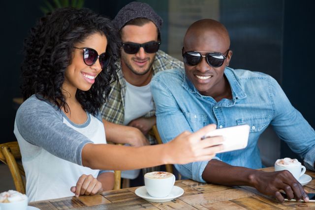 Happy multi ethnic friends wearing sunglasses while taking selfie in coffee shop
