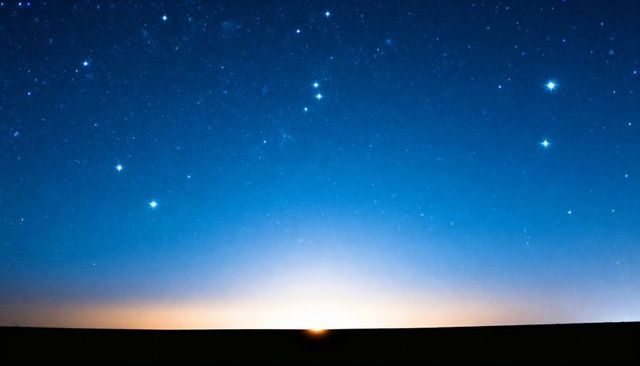 Starry dawn with rising sun over flat horizon, starlit sky transitioning to morning light