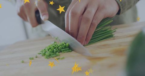 Closeup chopping chives with chef knife on wooden cutting board with gold star overlays