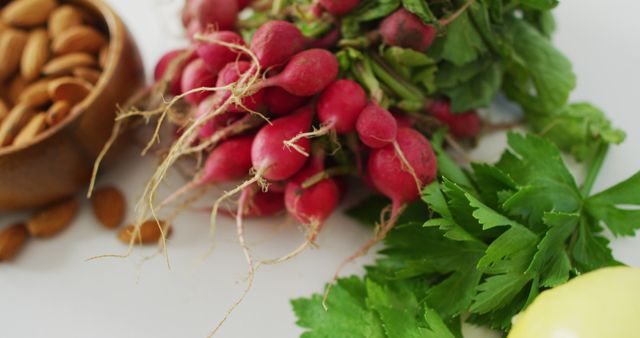 Close-up view showing fresh radishes, almond nuts in a wooden bowl, and herbs on white background. Ideal for use in articles or blogs about healthy eating, vegan diet, organic food farming, vegetarian recipes, kitchen ingredients, or clean eating advertising.