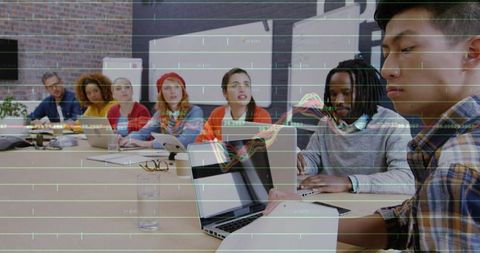 Young multicultural team collaborating around laptops with data visualization overlay in boardroom