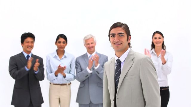 Group of professional coworkers standing and clapping as they congratulate a businessman celebrating a success in the workplace. Ideal for promoting diverse teamwork, business achievements, and positive work environments.