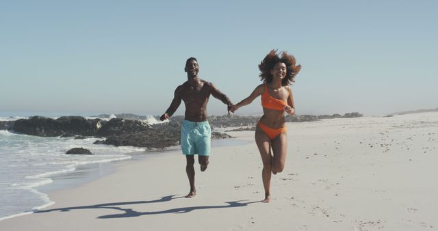 Couple running along sandy beach holding hands. Ideal for vacation promotions, summer holiday advertisements, travel blogs, active lifestyle content, and romantic getaway marketing materials.