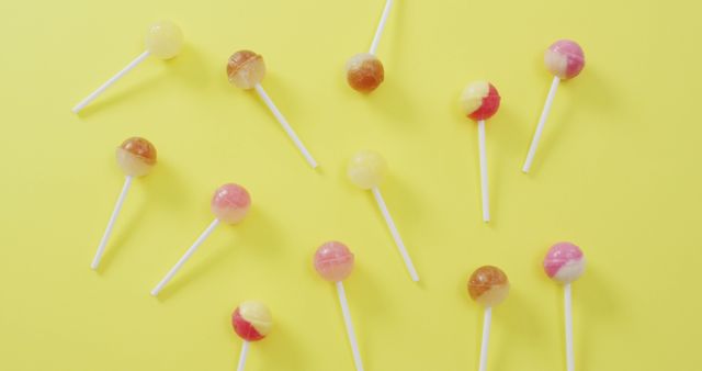 This image showcases an assortment of colorful lollipops scattered on a bright yellow background. Perfect for usage in advertisements for candy stores, dessert promotions, children-related content, and bright, vibrant graphic design projects. The fun and cheerful nature of the image attracts attention and adds a playful touch.