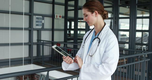 A young Caucasian female doctor reviews patient information on a tablet, with copy space. Her focused demeanor and professional attire underscore the importance of technology in modern healthcare.