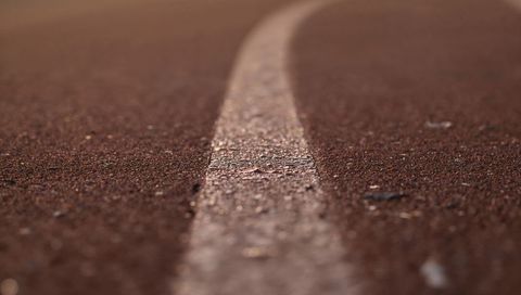 Curving white lane line on worn red rubber track macro texture for athletics