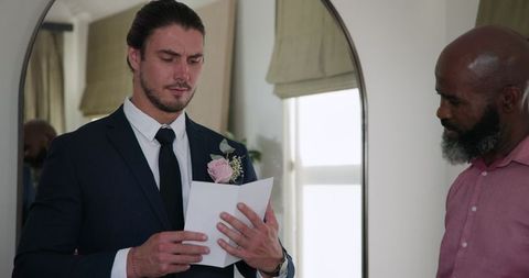 Groom Reading Note with Supportive Friend at Wedding