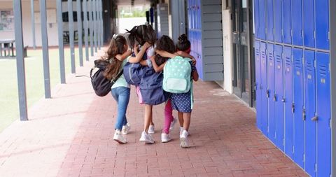 Happy Schoolgirls with Backpacks Walking Together in School Hallway