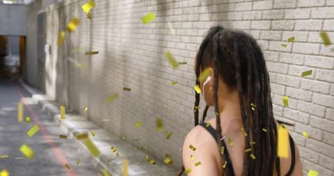 Woman with dreadlocks walking down brick alley with gold confetti and dynamic motion
